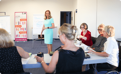 Fünf Frauen in einem Besprechungsraum, eine steht vor Flipcharts, die anderen sitzen an einem Tisch mit Papieren und Stiften.
