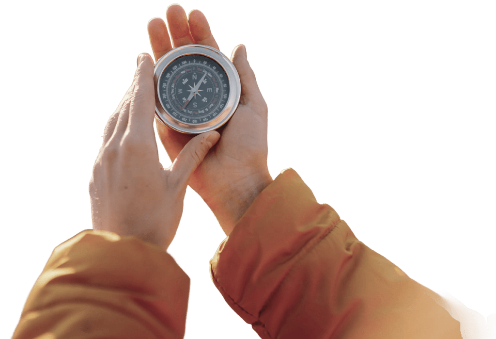 Zwei Hände in brauner Jacke halten einen Kompass mit schwarzem Zifferblatt und silbernem Rand.